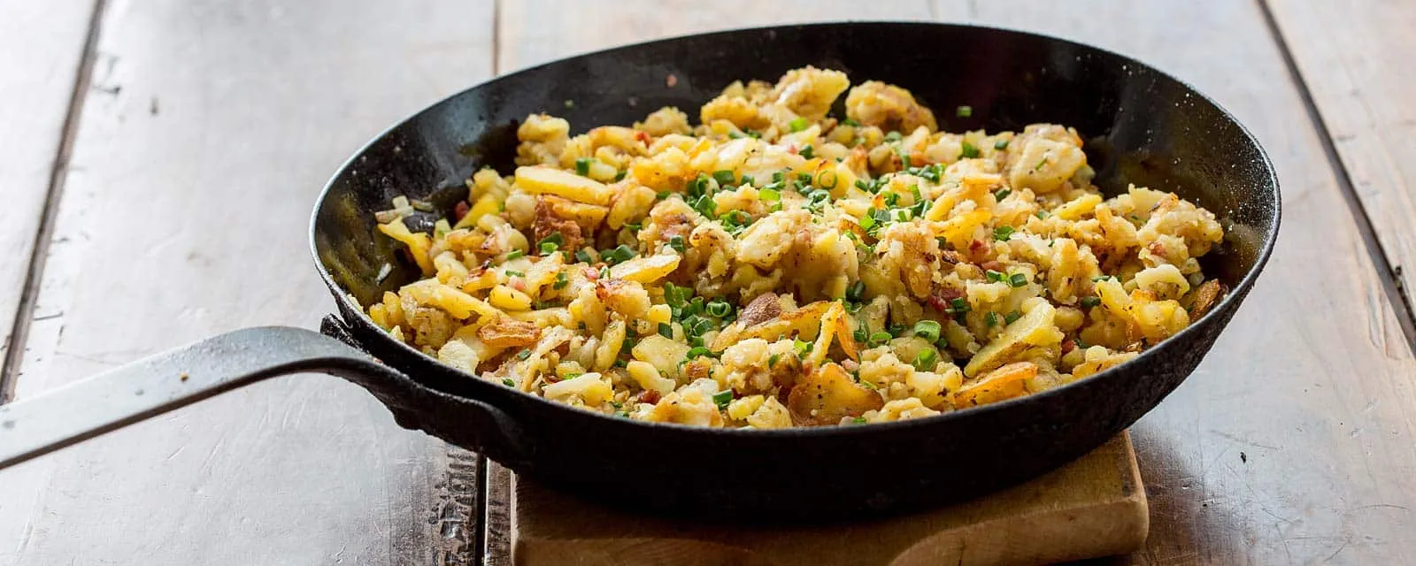 Bratkartoffeln in der gusseisernen Pfanne auf einem Holztisch