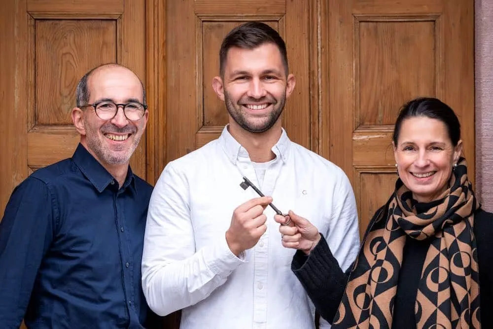 Schlüsselübergabe im Kartoffelhaus: die bisherigen Inhaber und der neue Inhaber vor der Holztür